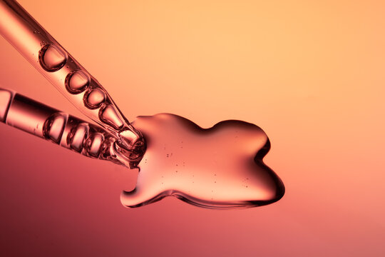 Close up of a pipette dispensing liquid on orange yellow background.
