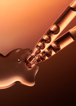 Close up of a pipette dispensing liquid on orange yellow background.