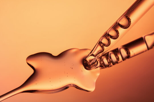 Close up of a pipette dispensing liquid on orange yellow background.
