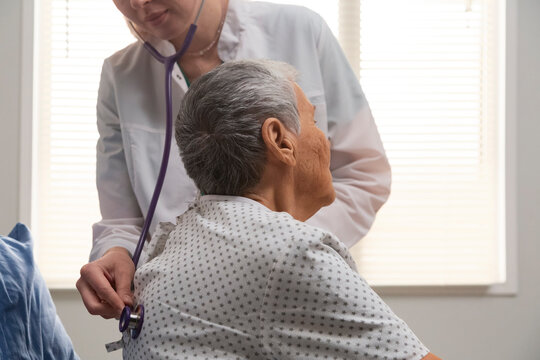 Doctor using stethoscope examining elderly patient in hospital room