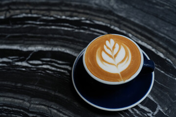 Latte art coffee in blue cup on black table.
