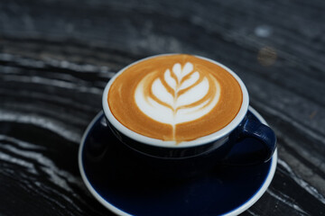Latte art coffee in blue cup on black table.