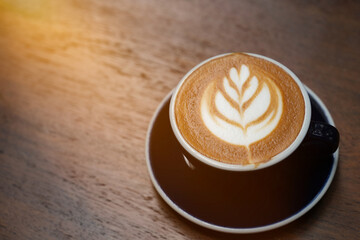 Latte art on a coffee cup on a wooden table in the warm sunlight.