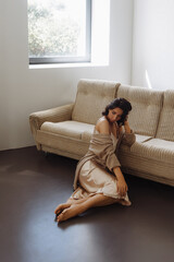 Obraz premium Young woman sitting on the sofa in the living room. Front view. Beige sweater thrown over shoulders.