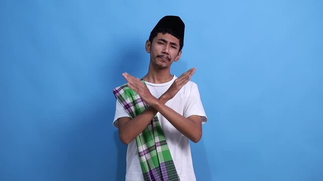 Serious young Asian Muslim man standing with Showing stop gesture with palm and thumbs down. People religious Islamic lifestyle concept