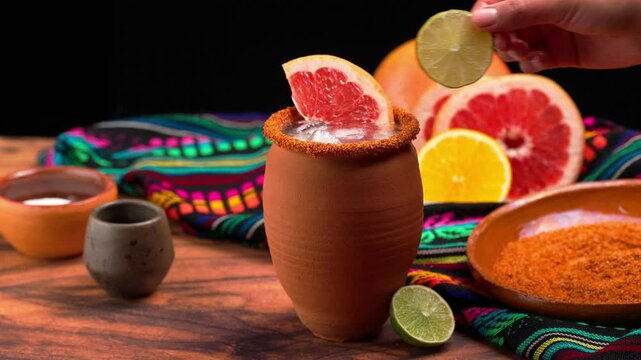 Tequila cantarito drink, a Mexican woman garnishes a cantarito cocktail with a slice of grapefruit and lime