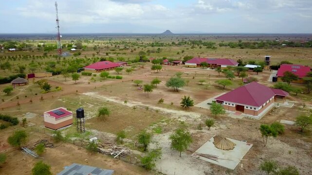 Aerial establishing shot capturing a vocational school in Karamoja, Uganda, featuring red-roofed buildings, solar panels, and water tanks amid a dry landscape, showcasing sustainable infrastructure