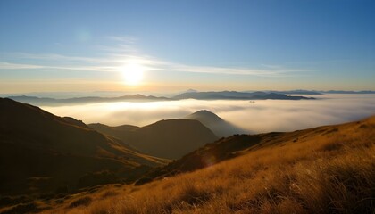 Sunrise over misty mountain range with golden grassy slopes, blue sky, and distant peaks fading into the horizon.