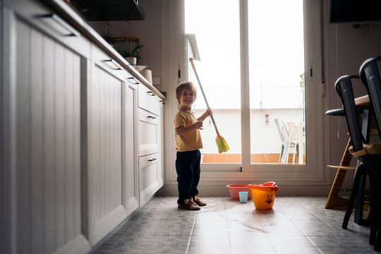 Young boy mopping floor with playful mop in bright kitchen