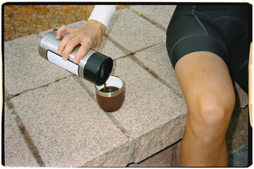 Flash-lit analog close-up of an anonymous cyclist preparing a coffee