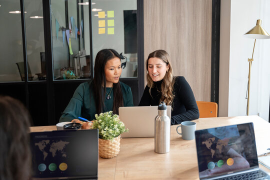 Businesswomen collaborating on laptop in modern office meeting room - Powered by Adobe