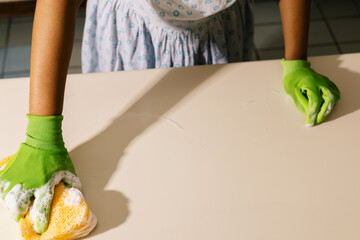 Anonymous hand cleaning a kitchen counter with green gloves