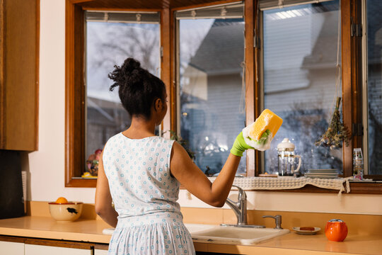 Young woman cleaning kitchen, holding up sudsy sponge