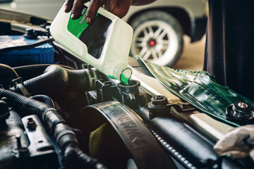 Male professional mechanic pouring antifreeze coolant liquid into car engine radiator in service...