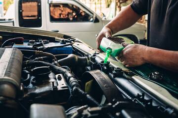Male professional mechanic pouring antifreeze coolant liquid into car engine radiator in service...