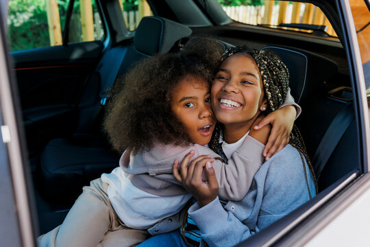 Two happy sisters hugging in back seat of car