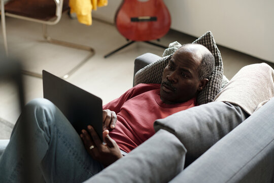 Black Freelancer Working on Laptop when Resting on Couch at Home