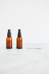 apothecary amber style moisturizer bottles next to blank labels with copy space on minimalistic white marble