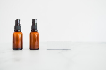 apothecary amber style moisturizer bottles next to blank labels with copy space on minimalistic white marble