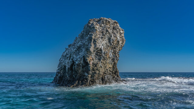 A lonely cliff in the blue sea. Steep rocky slopes against a clear azure sky. The waves are crashing against the rocks, foaming. Copy space. The Indian Ocean. Madagascar.