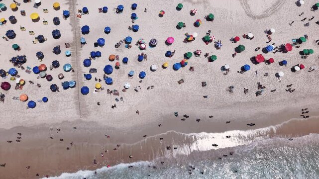 Aerial top down view showing people relaxing on the beautiful Copacabana Beach and coast on a bright sunny summer day. Slow motion drone view