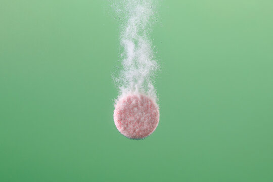 A Pink Tablet Dissolving in Water on Green Background