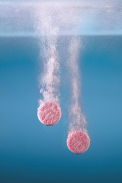 Two pink tablets creating fizzy bubbles as they dissolve against blue