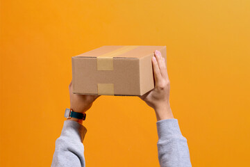 Hands Holding Cardboard Box Against Orange Background