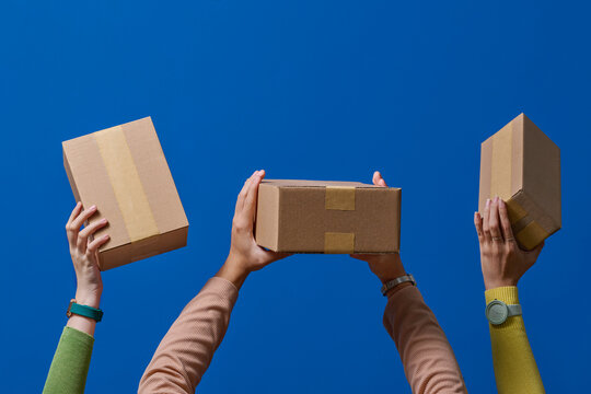 Hands Holding Cardboard Boxes Against a Vibrant Blue Background