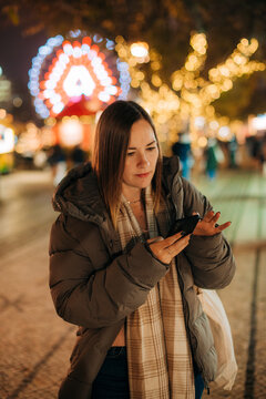 Woman texting on phone with festive lights in background