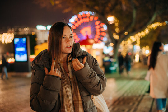 Woman recording audio message on festive street at night
