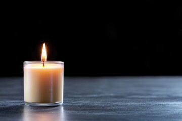 A single candle burns brightly in a glass holder on a smooth, dark surface. The warm light flickers gently, enhancing a peaceful ambiance, ideal for relaxation or meditation