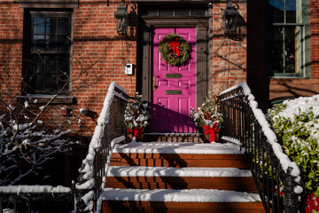 Snow-covered stairs and a pink door decorated with a Christmas wreath.
