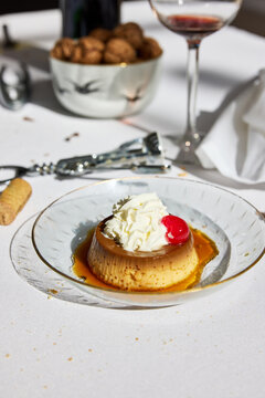 Flan dessert with whipped cream and cherry on a white table