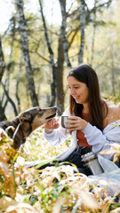 A sweet young woman with her dog enjoys the beauty of nature and the bond with her pets. The woman drinks tea from a thermos