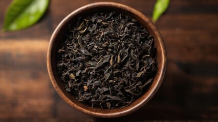 Dark and Mystical: Small wooden bowl filled with looseleaf black tea on wooden surface, with scattered leaves and blurred background.