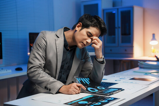 Stressed asian businessman having headache working with financial data at night