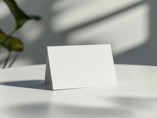 Minimalist White Invitation Card Mockup with Plant Shadow Overlay on Smooth Table Surface Closeup