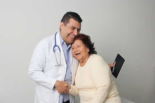 Elderly 80-year-old Latin woman visits the dark-skinned geriatric specialist medical doctor to check her health, they greet each other, laugh and hug