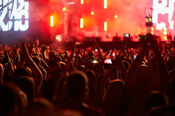 Energetic audience at summer music festival, hands raised, enjoying live concert. Stage lights...