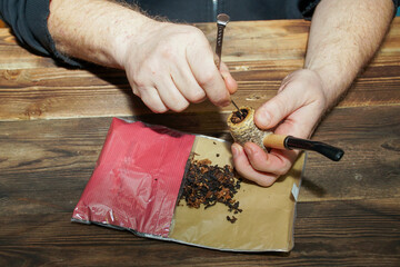 A man stuffs a smoking pipe with tobacco using a tamper.