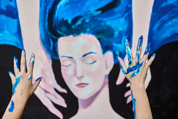 Adult woman with blue hair, depicted on canvas. Hands of young artist apply blue paint, enhancing...