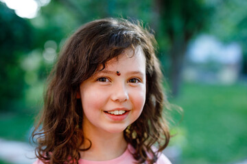 Fototapeta premium Portrait of little school girl with ladybug on face. Happy smiling excited child on warm summer sunny day.