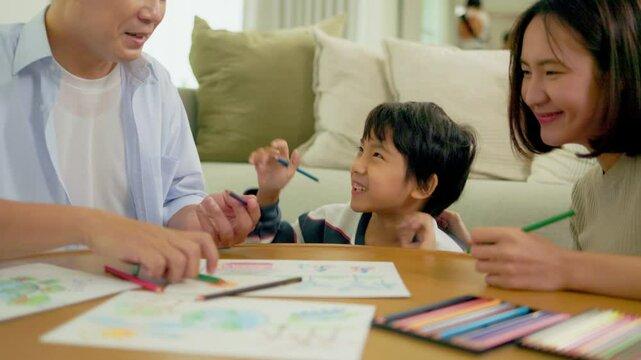 Happy Asian family drawing on paper together. Daughter with parent lying on floor and playing together in the living room at home. Love and bonding moment concept