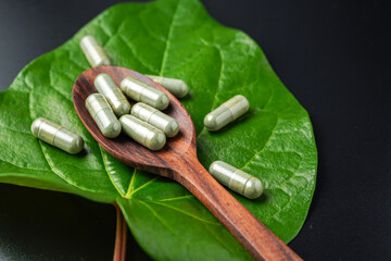 Pile of herbal capsules on wooden spoon with herbs and green natural Betel pepper leaf background