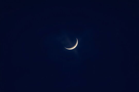 Bright crescent moon in a deep, clear night sky with scattered clouds evoking serenity. - Powered by Adobe