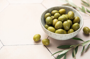 Green olives with olive branches resting in a bowl on a tiled surface