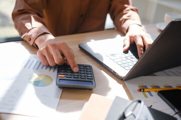 Accountant working on financial calculations using a calculator and laptop for business analysis.
