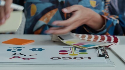 Close up shot of hands of unrecognizable female designer reviewing color swatches and sketches for vibrant logo design at well-organized desk in creative workspace