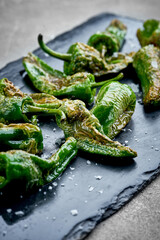 A vibrant and appetizing platter of roasted green peppers, seasoned with sea salt. The peppers are perfectly charred and have a glossy finish.
